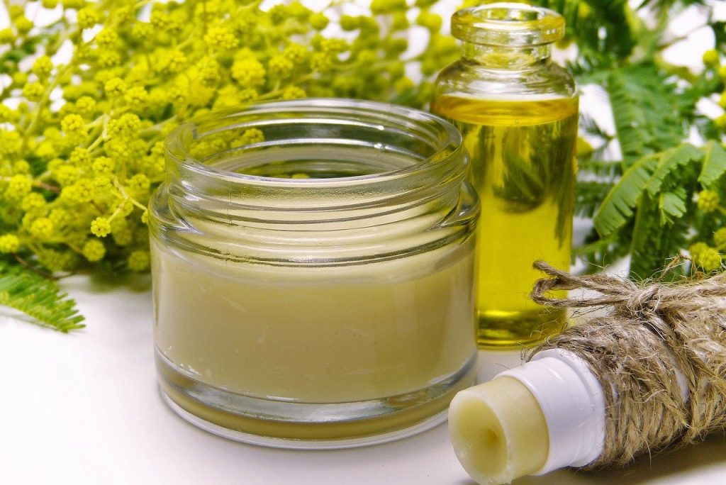 Pot de baume naturel et flacon d’huile essentielle avec fleurs jaunes en arrière-plan.
